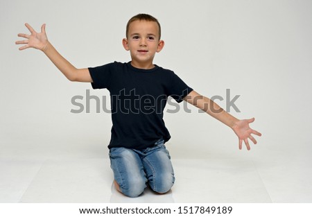 A full-length portrait of a cute boy child sitting on the floor on a white background with Vitiligo disease is a violation of the color of the skin at the initial stage. Black T-shirt, blue jeans.