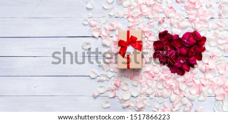 Gift box and heart shape created from red rose petals  out standing from light pink rose petals on white wooden background with copy space. Top view. Love concept. Gift time.
