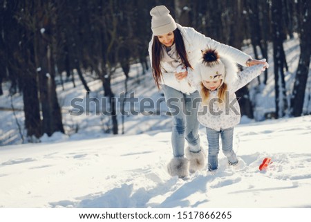 young and stylish mom with long dark hair playing with her little cute daughter in winter snow park