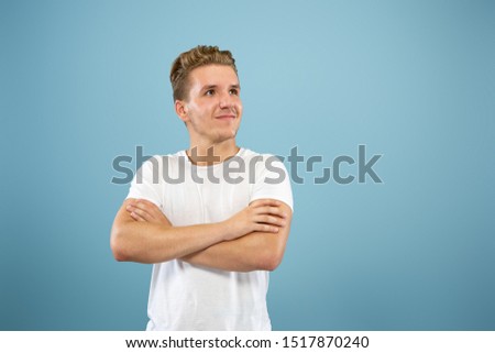 Caucasian young man's half-length portrait on blue studio background. Beautiful male model in shirt. Concept of human emotions, facial expression, sales, ad. Standing and smiling, looks confident.