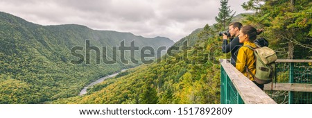 Travel couple hikers tourists taking photo with camera at view of mountain landscape in Autumn forest Parc de la Jacques Cartier, Quebec, Canada. Panorama banner background.