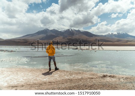 Tourist man with dramatic mountain landscape. Pretty wake lake landscape with mountain background. Mountain range view shot in Salt Flats of Uyuni, Bolivia. Copy space, blue sky and green foreground