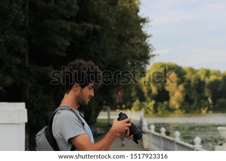 young guy looking and his camera after making photos, male profile portrait in park outdoor environment, photography hobby concept picture 