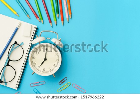 Flat lay photo of office desk with colorful pencil, Paper clip, Glasses, Note book, White retro clock, Top view of the copy space
