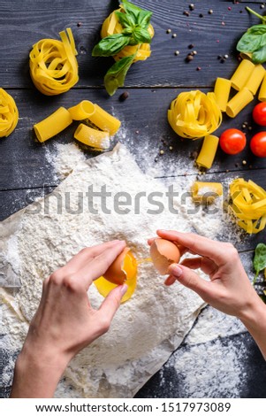 Close up of chef's hands with plain flour well and eggs in preparation process for baking, cooking, pastry making. Woman breaks eggs in flour. Adding egg yolk to cooking