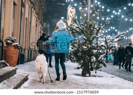 Woman walking down with white dog by alley.