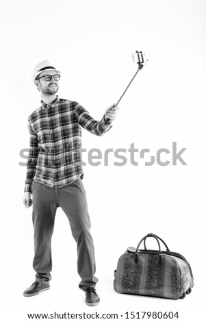 Full body shot of happy young man smiling while holding selfie stick and taking selfie picture with mobile phone ready for vacation