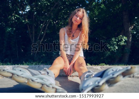 young woman sits on the pavement in the park in roller skates