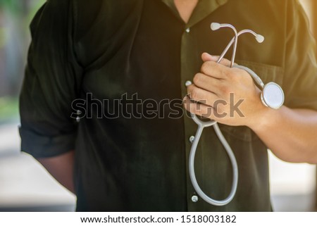 The medical doctor wearing dark shirt is holding his stethoscope in his hand with flare at the scope with intention. 