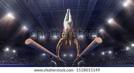 Male athlete doing a complicated exciting trick on parallel bars in a professional gym. Man perform stunt in bright sports clothes