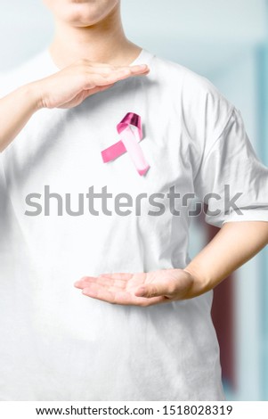Woman in a white shirt showing pink awareness ribbon in the hospital background. Breast cancer awareness