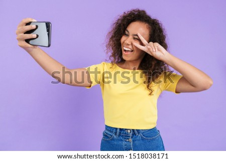 Lovely happy young african girl wearing casual clothing standing isolated over violet background, taking a selfie, showing peace gesture