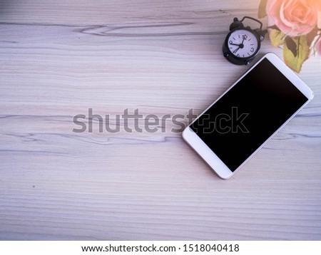 Top view phone on wooden desk with alarm clock in home.