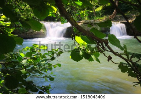 Waterfalls on a mountain river in the forest behind green leaves, mountain stream in Poland