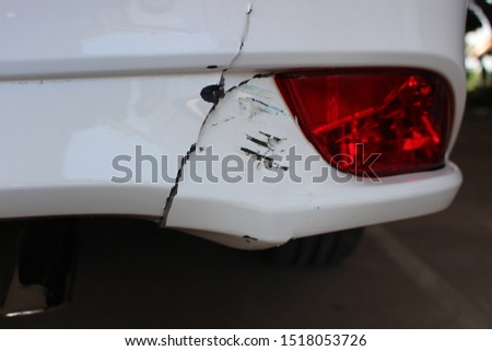 The rear bumper of a white car has cracks due to an accident on the road
