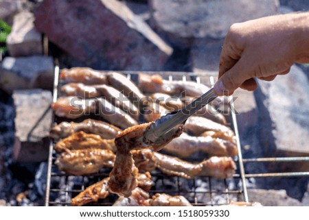 Hands of man preparing barbecue steaks and chicken meat on the grill. People cooking tasty food on barbecue grill outdoors,close-up.Grilling at summer weekend. Fresh meat preparing on grill for lunch.