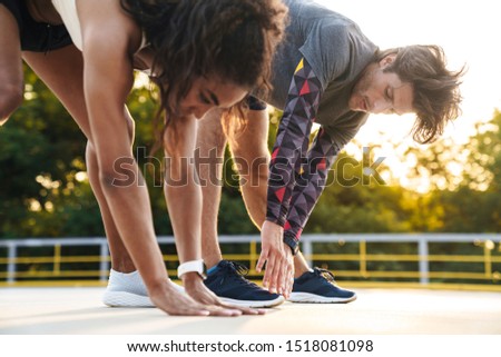 Photo of young strong sports couple man and woman make stretching exercises outdoors.