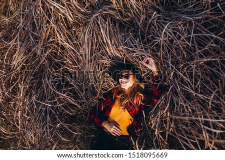 Portrait of a girl in a black hat on a background of autumn nature. The blonde walks through the autumn forest. The girl in the red jacket is sitting on the mowed grass. girl in stylish autumn look.