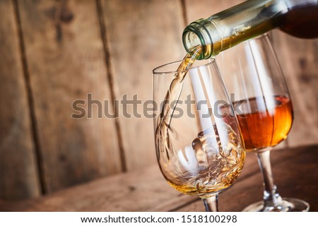 Dispensing golden sherry, a speciality from Andalusia, Spain, into wineglasses in a close up on the neck of the bottle over wood with copy space
