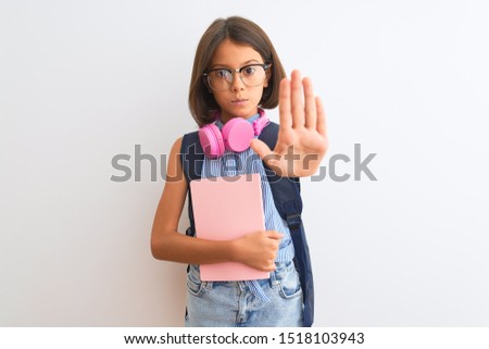 Student child girl wearing backpack glasses book headphones over isolated white background with open hand doing stop sign with serious and confident expression, defense gesture
