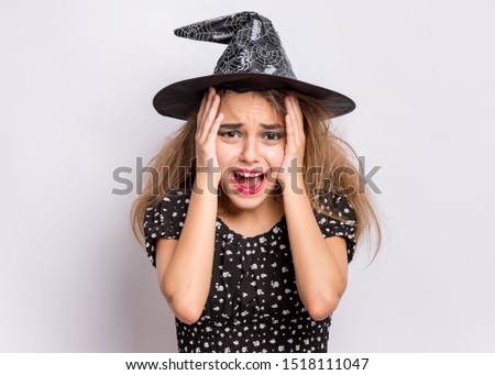 Happy halloween concept. Surprised Teen girl in witch black hat posing on grey background. Shocked young teenager in witch halloween costume, looking at camera.