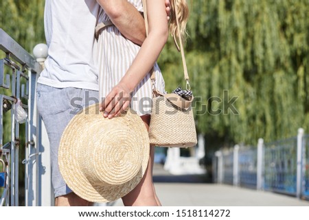Close-up picture of young couple's legs on romantic date. Two people embracing each other, standing on the bridge, Woman's hand, holding straw hat and hugging a man.