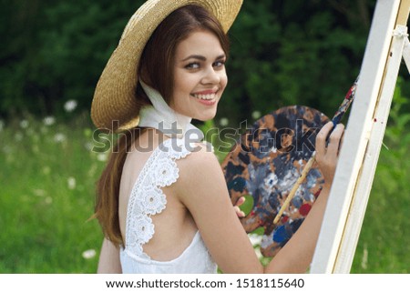 young woman looking at the camera an easel in a hat