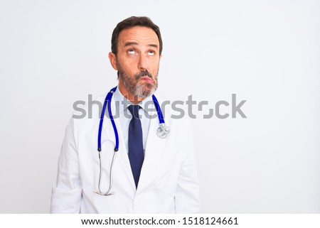 Middle age doctor man wearing coat and stethoscope standing over isolated white background making fish face with lips, crazy and comical gesture. Funny expression.
