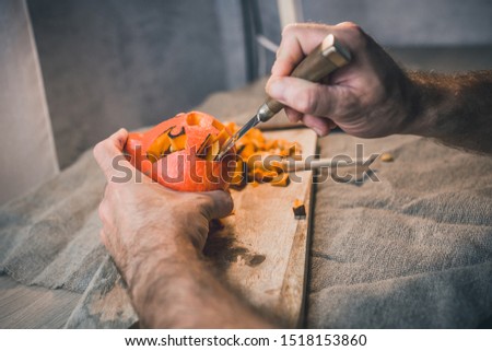A man cuts out his mouth in a pumpkin head preparing for Halloween
