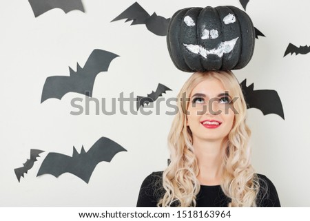 Cheerful young woman smiling and looking up at black painted pumpkin on her head
