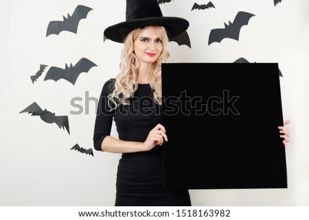 Pretty smiling young woman in witch costume holding empty blackboard
