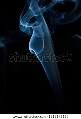White and blue curly twirling smoke trails appearing on a dark black background 