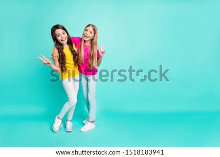 Full length body size photo of two ecstatic excited encouraged girlfriends showing you v-sign while isolated with teal background