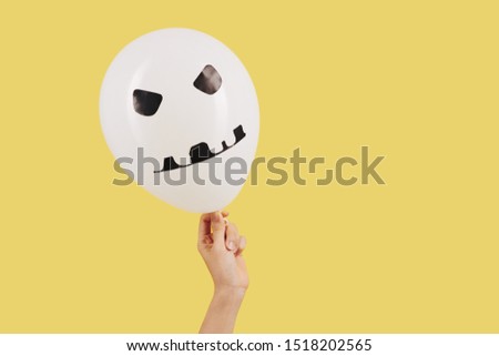 Person holding white balloon with scull looking sticker, isolated on yellow background