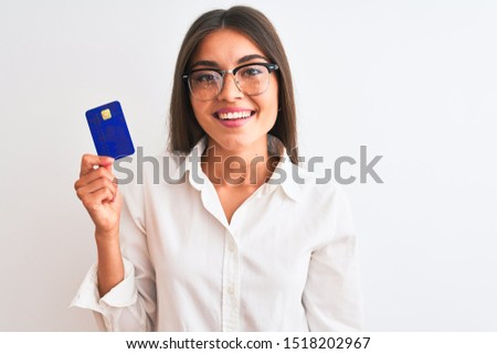 Young businesswoman wearing glasses holding credit card over isolated white background with a happy face standing and smiling with a confident smile showing teeth