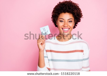 Photo of cheerful cute nice fascinating youngster smiling toothily wearing white striped sweater holding piece of paper with emoji on isolated pink color background pastel