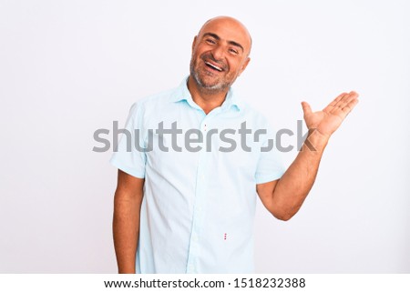Middle age handsome man wearing casual shirt standing over isolated white background smiling cheerful presenting and pointing with palm of hand looking at the camera.