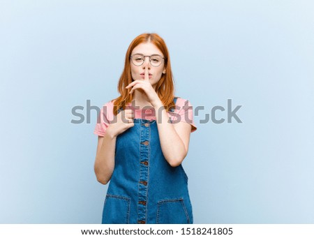 young red head pretty woman looking serious and cross with finger pressed to lips demanding silence or quiet, keeping a secret