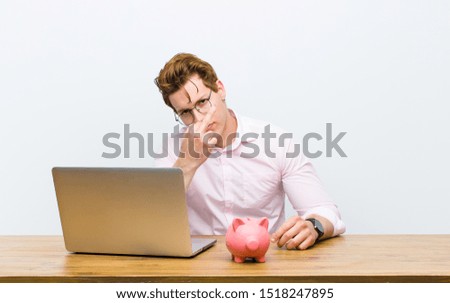 young red head businessman working in his desk with a piggy bank