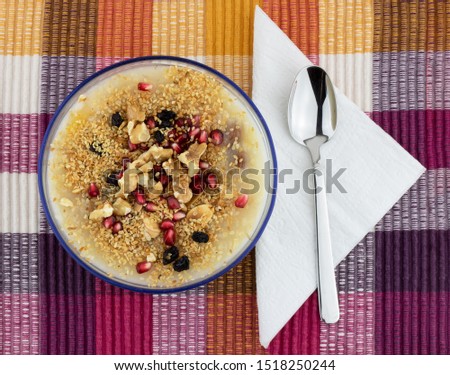 Traditional Turkish dessert called "Aşure" also known as Ashura, Asure or Ashure or Noahs Pudding. Healty meal with dried fruits, walnut and pomegranade. Flat lay food on colorful background. Royalty-Free Stock Photo #1518250244