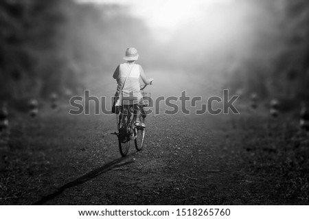 A black and white image of a woman riding a bike alone in a dirt road at night