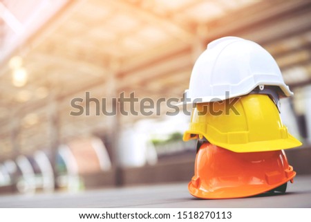 orange yellow and white hard safety wear helmet hat in the project at construction site building on concrete floor on city with sunlight. helmet for workman as engineer or worker. concept safety first