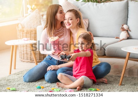 Happy lesbian couple with little daughter playing video game at home
