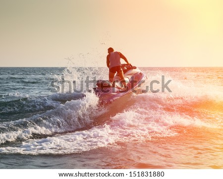 Silhouette of strong man jumps on the jetski above the water at sunset