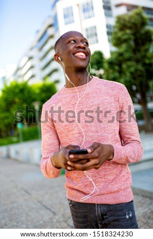 Portrait of happy young african man listening to music with cellphone and headphones 