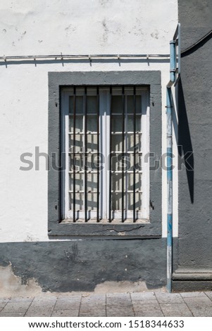 White facade of a house with a window with grill and a grey frame. Traffic sign on the right. Strong sunlight. Ribeira Grande, Sao Miguel, Azores Islands, Portugal.