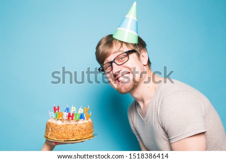 Crazy funny positive guy hipster with a happy birthday cake standing on a blue background. Concept of jokes and holiday greetings.