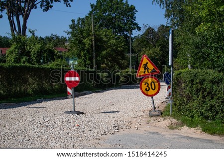 A street view with a gravel road under construction and road signs of access prohibited, speed limit 30, road works Royalty-Free Stock Photo #1518414245