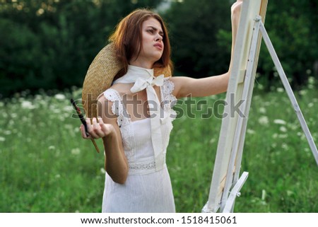 woman looks at a white canvas with a brush in her hands an easel