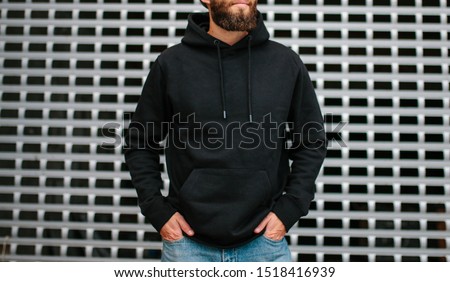 City portrait of handsome hipster guy with beard wearing black blank hoodie or sweatshirt and hat with space for your logo or design. Mockup for print Royalty-Free Stock Photo #1518416939